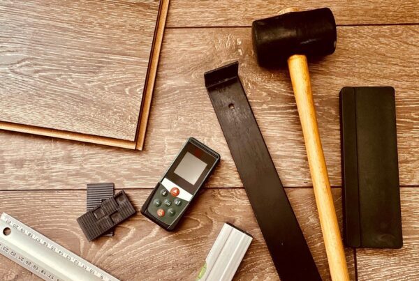 Gereedschap en materialen voor laminaat leggen op houten vloer, waaronder hamer en afstandhouders