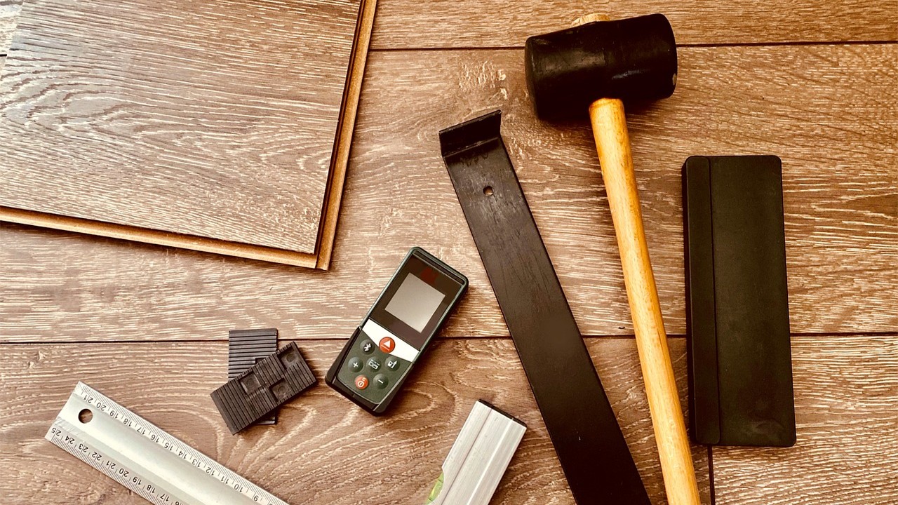Gereedschap en materialen voor laminaat leggen op houten vloer, waaronder hamer en afstandhouders