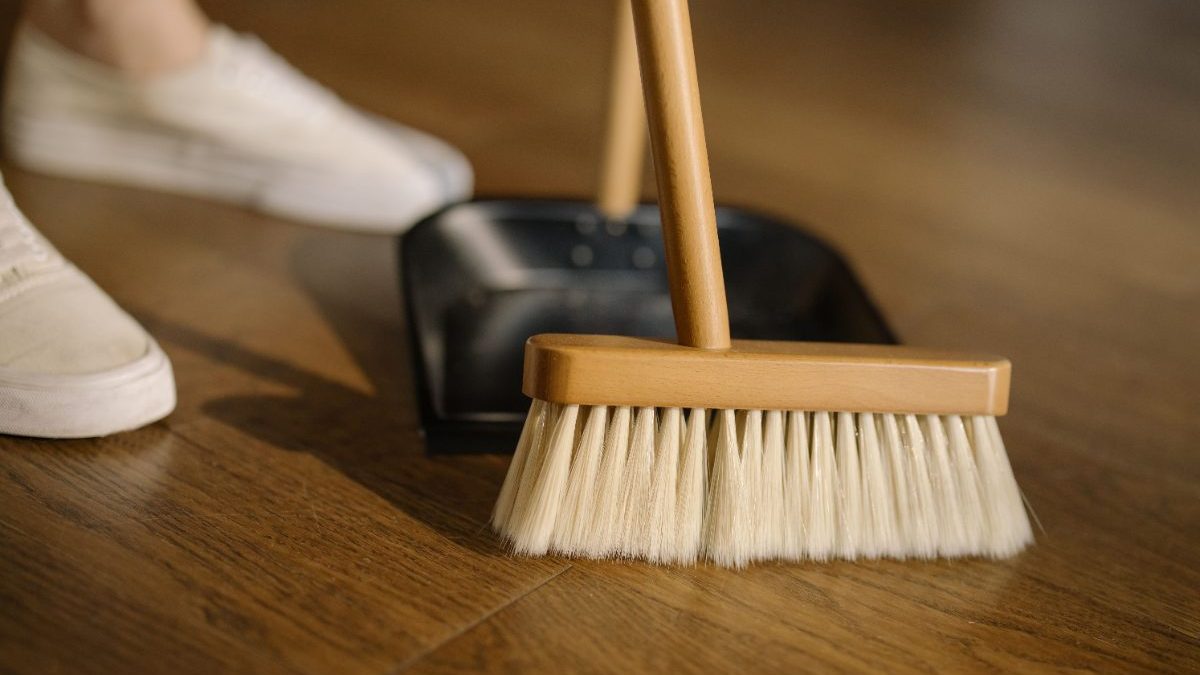 Parketvloer schoonvegen met een zachte bezem en stoffer om zand en stof te verwijderen